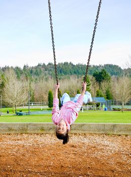 Happy little nine year old part Asian girl swinging upside down