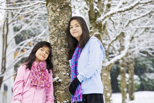 Two young girls standing by tree in fresh snow