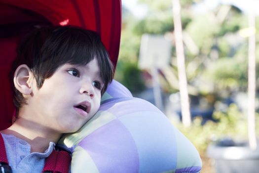 Cute four year old boy looking quietly off to side while sitting in stroller