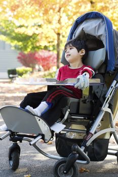 Disabled boy with cerebral palsy in medical stroller enjoying an autumn day outdoors at the park