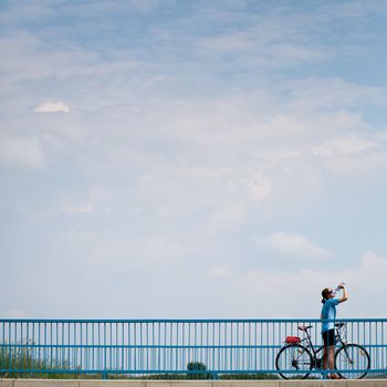 Background for poster or advertisment pertaining to cycling/sport/outdoor activities - female cyclist during a halt on a bridge against blue sky (color toned image)