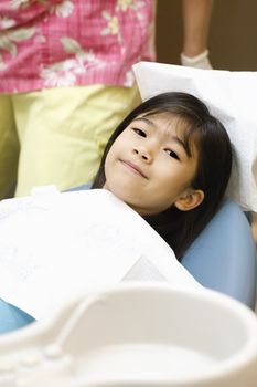 Little Asian girl sitting in dentist's chair ready for cleaning