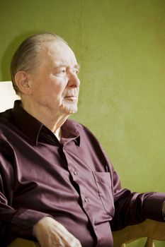 Elderly man in rocking chair looking out sunny window