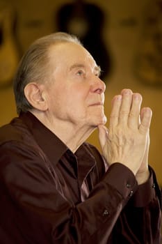 Elderly man looking up while oraying in dark church