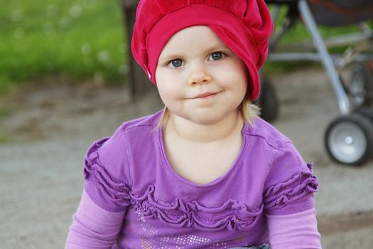 Cute toddler girl with red hat on playground