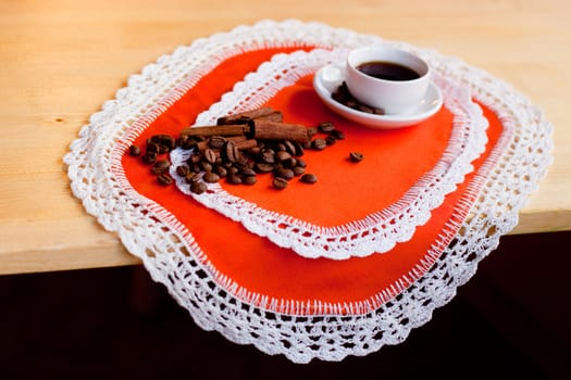 A coffee cup and coffee beans and several cinnamons on two orange napkins
