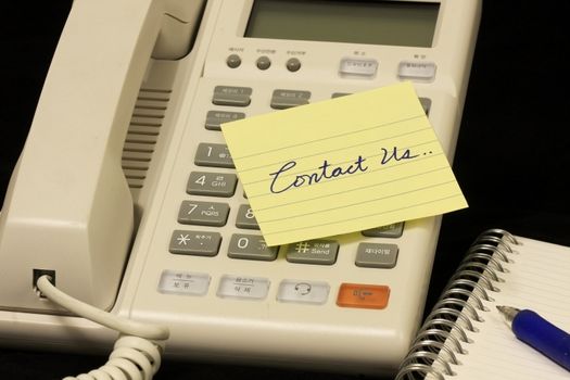 yellow message note over a phone in a writing contact us!
