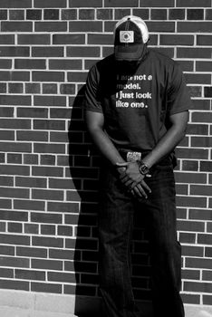 Attractive young African American male playing posing in a t-shirt and jeans against a brick wall.