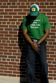 Attractive young African American male playing posing in a green t-shirt and jeans against a brick wall.