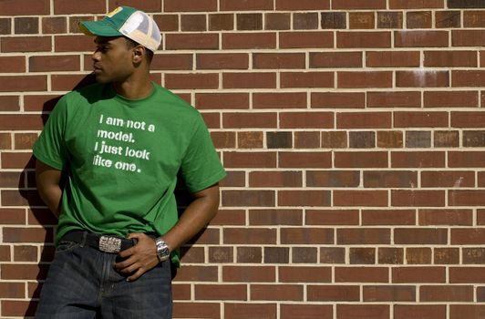 Attractive young African American male playing posing in a green t-shirt and jeans against a brick wall.