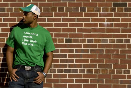 Attractive young African American male playing posing in a green t-shirt and jeans against a brick wall.