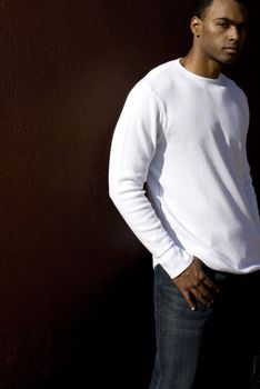 Attractive young African American male playing posing in a white t-shirt and jeans against a solid brown wall.