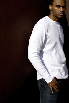 Attractive young African American male playing posing in a white t-shirt and jeans against a solid brown wall.