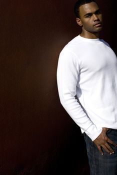 Attractive young African American male playing posing in a white t-shirt and jeans against a solid brown wall.