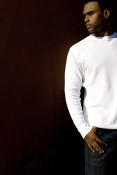 Attractive young African American male playing posing in a white t-shirt and jeans against a solid brown wall.