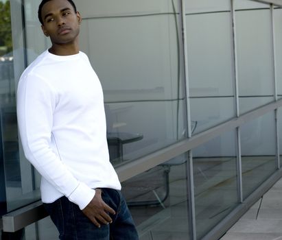 Attractive young African American male playing posing in a white t-shirt and jeans against a glass.
