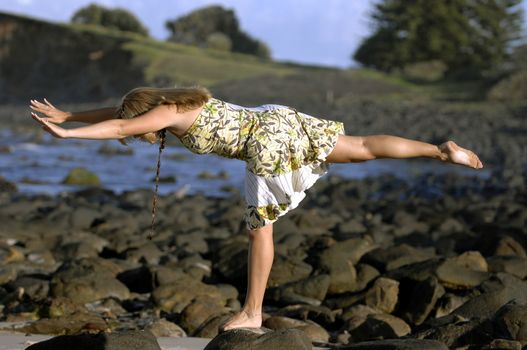 A beautiful young woman practices yoga on a the beach