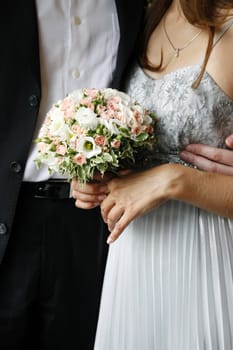 Bouquet of flowers on a background of a dress of the bride and a suit the groom.