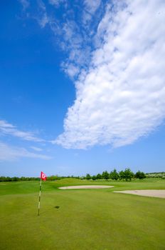 Golf course and flag. Blue and cloudy sky.