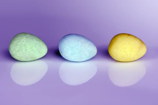 Pastel colored Easter egg candy in a row on purple background with reflection and copy space for your text.