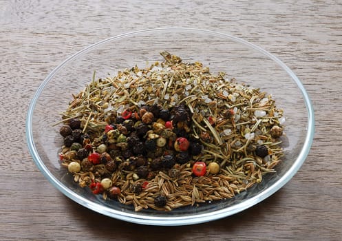 Mix of spices in glass saucer isolated on dark wooden table