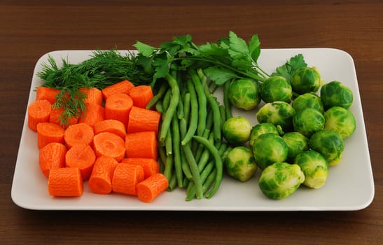 Mix of vegetables including chopped carrots, Brussels sprouts, green beans and dill on rectangular grey ceramic dish