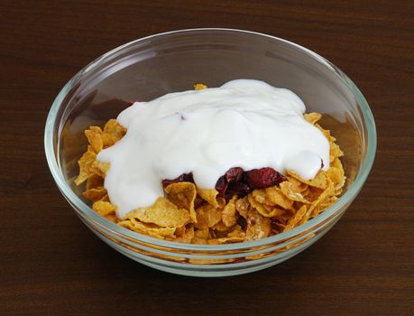 Cornflakes with dried cranberries and yogurt in glass bowl on dark wooden table