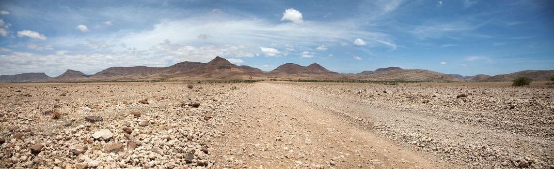 Surreal panorama of the Kaokoland game reserve in Namibia, sand track going toward the Skeleton Coast Desert with a blue sky