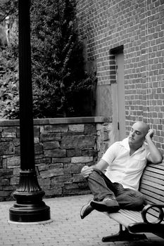 A man in his twenties sitting casually on a bench in an urban area.