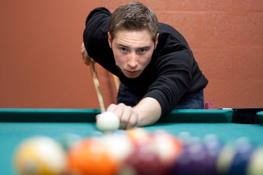 A young man lines up his shot as he breaks the balls for the start of a game of billiards. Shallow depth of field.