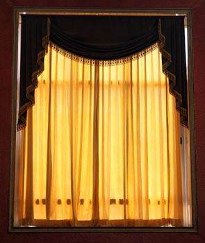 A window with beautiful yellow curtains inside a hall.