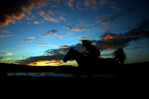 A horserider in speed on the backdrop of the twilight sky.