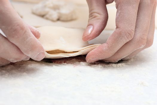 Pair of hands making pastry with dough.