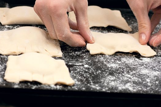 Pair of hands laying out raw pastries on a baking tray