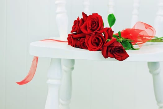Beautiful long stem roses with ribbin on a white chair against a white wall.