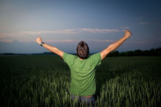 Young man enjoying his freedom/rejoicing from his success in the countryside, in a wheat field at dusk