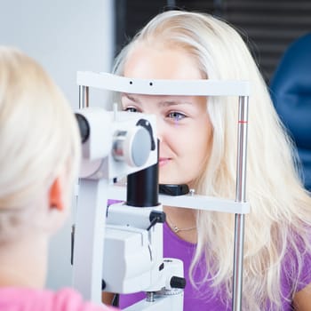 optometry concept - pretty, young female patient having her eyes examined by an eye doctor (color toned image; shallow DOF)