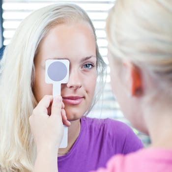 optometry concept - pretty, young female patient having her eyes examined by an eye doctor (color toned image; shallow DOF)