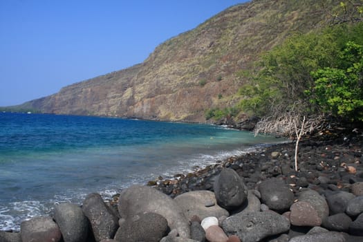 black rocks on an oceanside beach with a mountain in the background