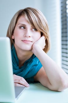 Portrait of a young woman pensively looking out of the window while sitting in front of her laptop