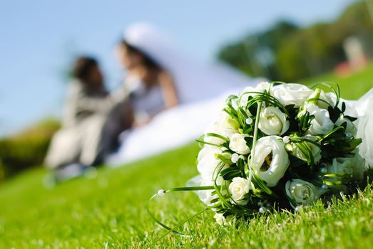 bridal bouquet of white roses on a green meadow and blurred newlyweds