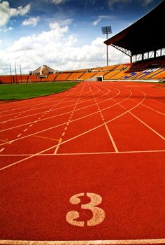 Running track number in front of tracks and stadium with blue sky and white cloud.