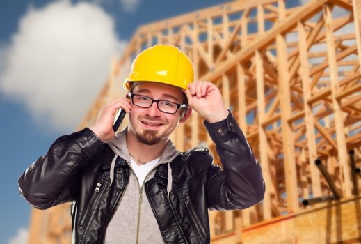 Young Contractor Wearing Hard Hat on Cell Phone In Front of Construction Site.