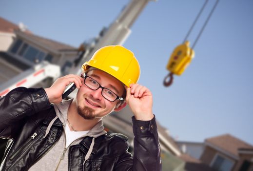 Young Contractor Wearing Hard Hat on Cell Phone In Front of Utility Crane.