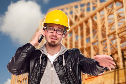 Young Contractor Wearing Hard Hat on Cell Phone In Front of Construction Site.