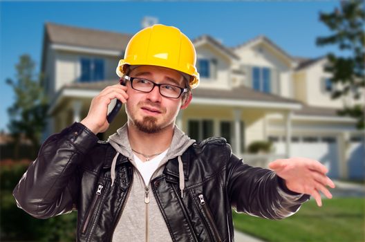 Young Contractor Wearing Hard Hat on Cell Phone In Front of House.