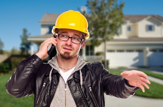 Young Contractor Wearing Hard Hat on Cell Phone In Front of House.