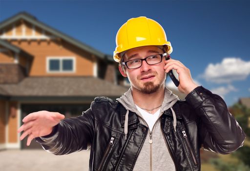 Young Contractor Wearing Hard Hat on Cell Phone In Front of House.