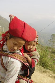 Nearly SAPA, City of North Vietnam. A woman of the ethnic (minority) Hmong Red pompoms with her baby in the back. She wears her beautiful costumes and hairstyle typical. Her baby was also a traditional cap color