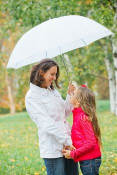 Cute girl with her mother with white umbrella walking in the autumn park. Rain, yellow leaves, tree.